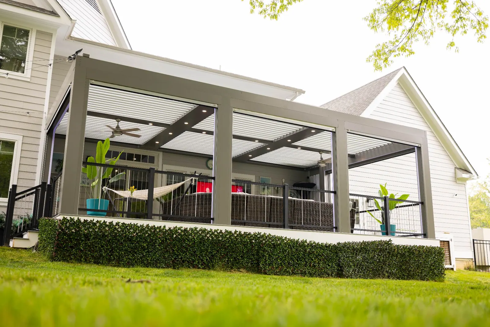 Light gray louvered pergola attached to a home above a raised patio