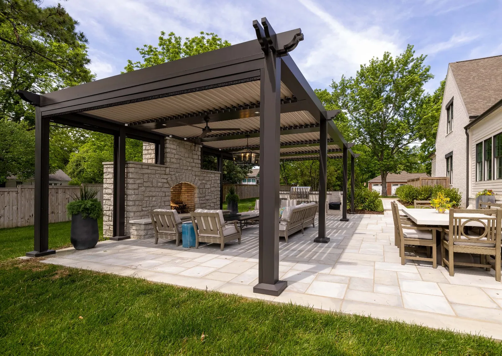 Dark louvered pergola covering lounge seating beside a stone fireplace