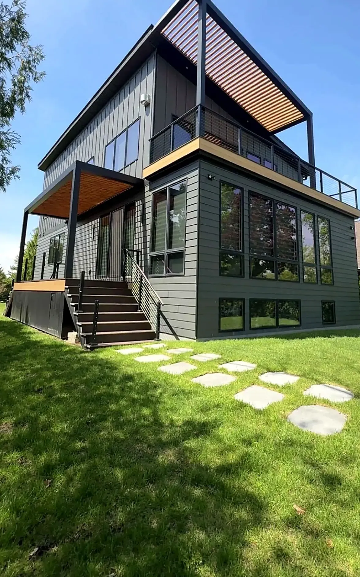 Modern dark-clad lakehouse in Fond du Lac with two louvered pergolas and cable railing