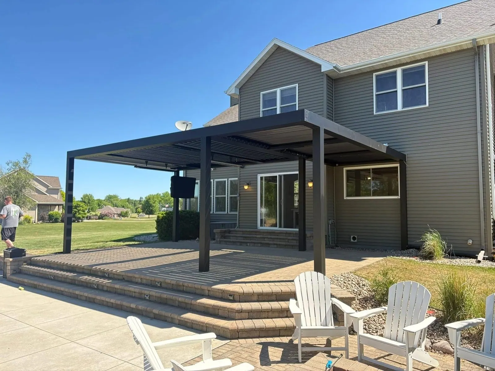 Black louvered aluminum pergola shading a paver patio behind a Fond du Lac home