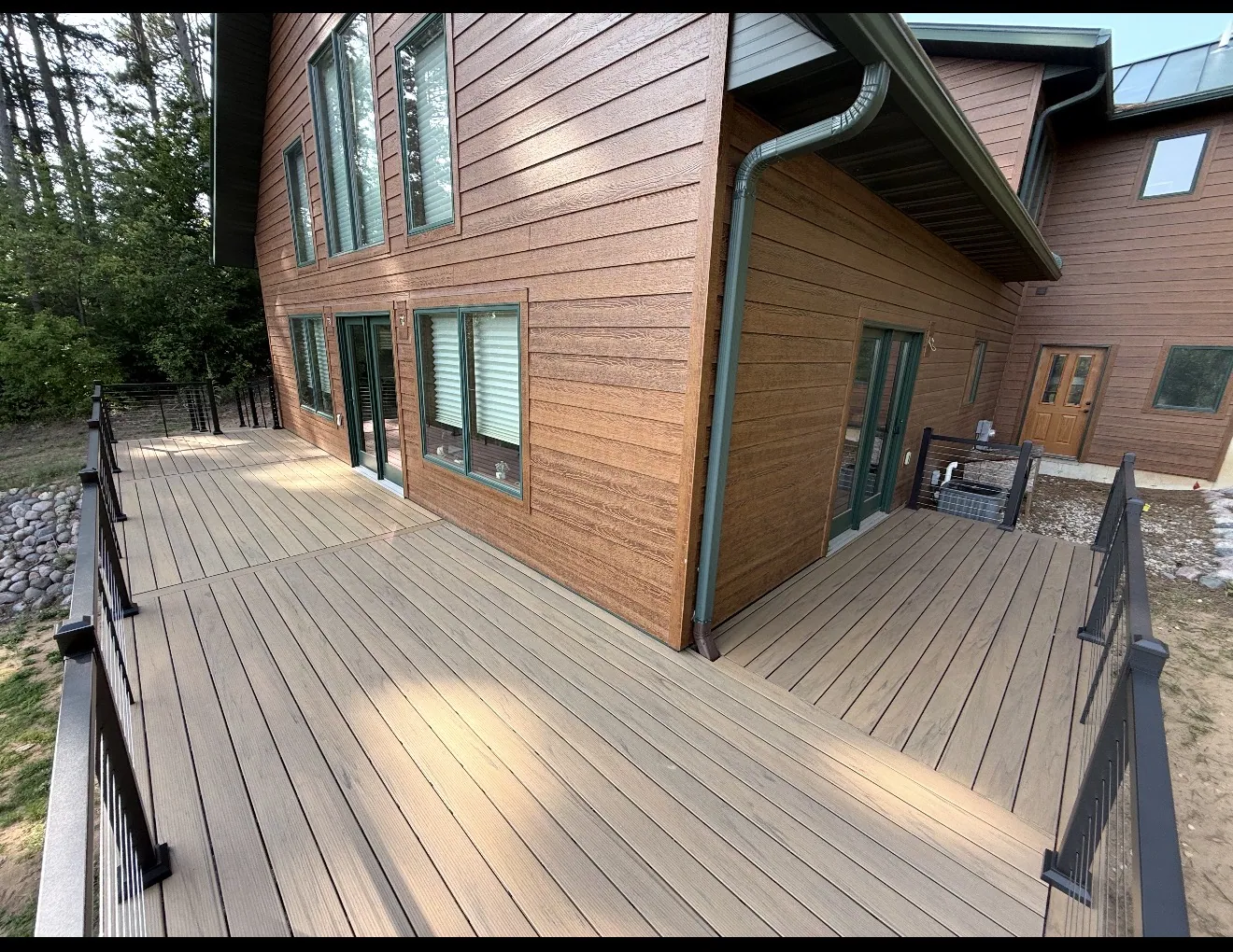 Custom composite deck with cable railings wrapping a brown-sided Marion home