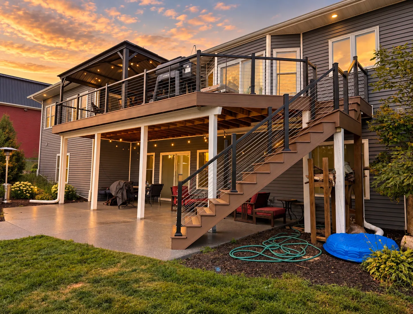 Two-story composite deck at sunset with a covered upper porch, cable railing, and a staircase in Plymouth, Wisconsin