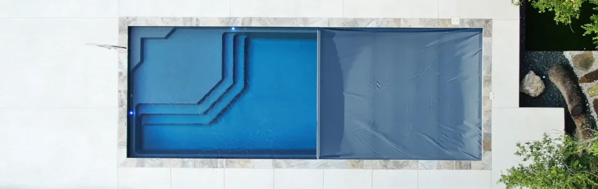 Automatic pool cover retracting over a fiberglass swimming pool